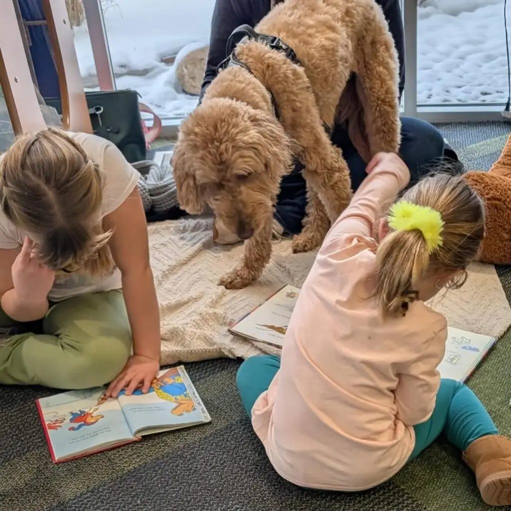 2 girls reading aloud to a dog